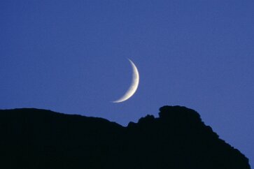 Crescent Moon The moon, about to drop behind the mountain peaks. It will continue to illuminate the sky until it sets below the horizon. Glacier Park MT 23 July 2001