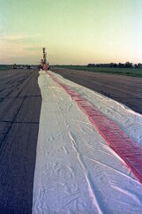19770500 Balloon Launch T11-10 The balloon is still inside a red wrapper, and laid out on a white tarp protecting it from any sharp debris on the runway.