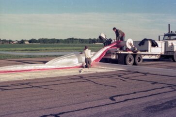 19770500 Balloon Launch T11-13 The balloon is threaded under a smooth spool, which will later spring open to release it. The top of the balloon is now removed from the red wrapper and a...